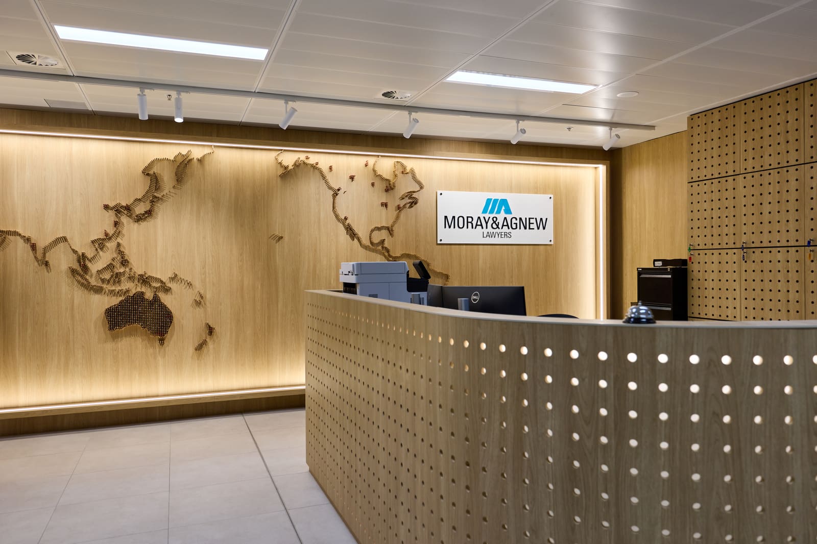 The reception desk of a law firm, in pale timber, with a world map made of small pegs on the wall behind it.