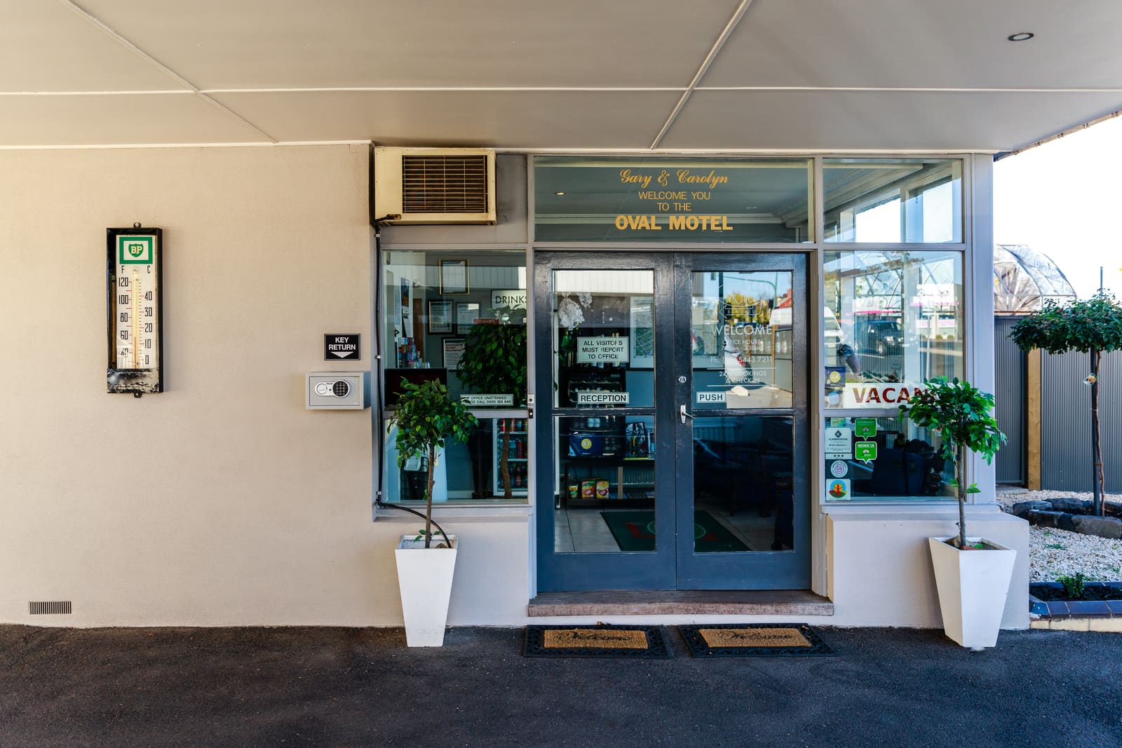 The front door of a motel reception, with a welcome sign above it, a vacancy sign in the window and a key return box on the wall.